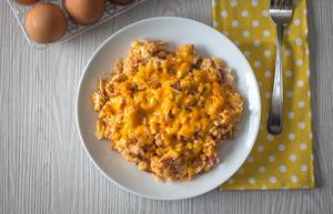 Scrambled eggs with red onions and cheese on a plate with eggs and a fork aside - top view