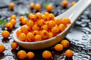 Sea buckthorn berries with water drops in white ceramic spoon on black background (Flip 2019)