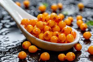 Sea buckthorn berries with water drops in white ceramic spoon on black background