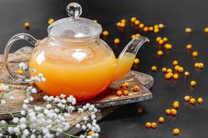 Sea buckthorn hot drink in a teapot with fresh berries on a black background (Flip 2019)