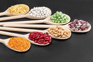 Set lentils, chickpeas, peas and beans of different colors in wooden spoons on black background