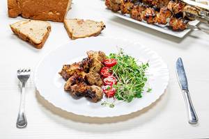 Shashlik with micro greens radish and tomato slices on a white wooden table with a knife and fork
