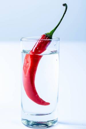 Shot of vodka and red hot chili pepper on white background