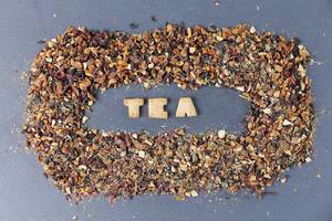 Sicht von oben auf das Wort "Tea", umrahmt von farbenfrohem, getrocknetem Tee