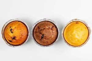Sicht von oben auf drei Muffins aus Schokolade, Karamell und Vanille, vor weißem Hintergrund