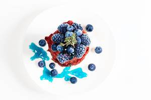 Sicht von oben auf einen Stapel Pfannkuchen aus Rote Bete Teig, dekoriert mit verschiedenen blauen Beeren, auf einem weißen Teller