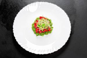 Sicht von oben auf Salat mit frischem Gemüse und Zwiebelsprossen auf einem weißen Teller