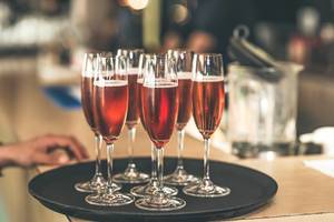Sieben rote Cocktails in Champagnergläsern auf einem schwarzen Tablett auf einer Theke