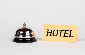 Silberne Hotelglocke neben Schild mit Wort HOTEL vor weißem Hintergrund