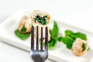 Slice of chicken roll with spinach on a fork close-up