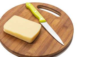Slice of yellow cheese on the kitchen wooden board with knife