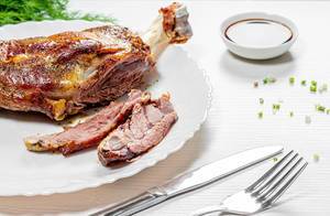 Sliced baked lamb meat on white wooden background with knife and fork (Flip 2019)