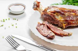 Sliced baked lamb meat on white wooden background with knife and fork