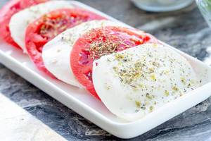 Sliced mozzarella cheese and tomatoes with dried Italian herbs on a plate (Flip 2019) (Flip 2019)