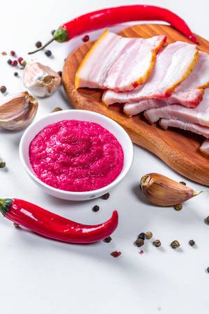 Sliced smoked bacon with horseradish sauce and spicy spices on white background