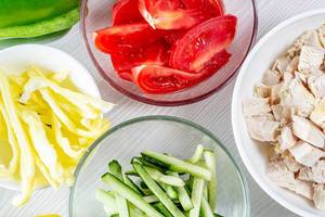 Sliced tomatoes, cucumbers, peppers and chicken fillet in glass bowls