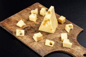 Slices of fresh Maasdam cheese on an old wooden kitchen board (Flip 2020)