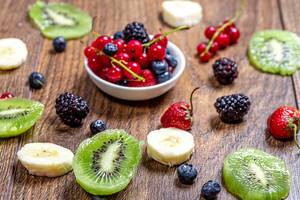 Slices of kiwi and banana, strawberry, currant, mulberry and currant on wooden background (Flip 2019)