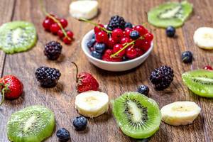 Slices of kiwi and banana, strawberry, currant, mulberry and currant on wooden background