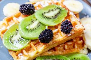 Slices of kiwi and banana with mulberry on Belgian waffles close-up