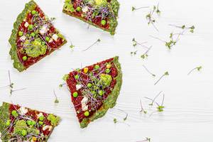 Slices of vegetarian vegetable pizza with micro-green cabbage on a white wooden background. Top view (Flip 2019)