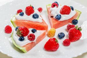 Slices of watermelon with cream and fresh berries on a white plate