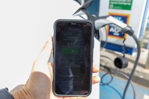 Smartphone-App zeigt den Ladebalken in km an, während  das Tesla E-Auto auf einem Aldiparkplatz mit Sonnenenergie geladen wird