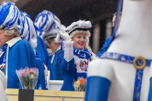 Smiling lady in the typical blue and white costume, wig and hat of the Blaue Funken throws sweets from the float of the traditional carnival society at the Rose Monday parade in Cologne