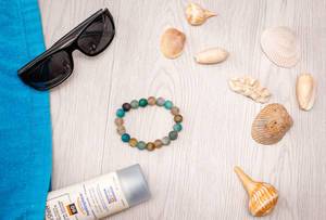 Sonnenbrille, Muscheln, Sonnencreme und Armband aus der Vogelperspektive