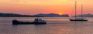 Sonnenuntergang hinter Bergen und zwei Schiffe auf der ruhigen See des argolischen Golfs vor Spetses, Griechenland