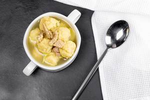 Soup with meat and dumplings on a black background with a white kitchen towel, top view