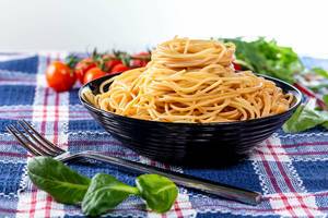 Spaghetti-Nudeln in einer schwarzen Schale angerichtet, mit Basilikum-Kräuter und Tomaten auf einem blauen Geschirrtuch
