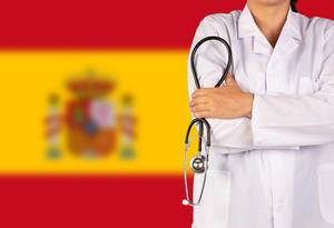 Spanisches Gesundheitssystem symbolisiert durch die Nationalflagge und eine Ärztin mit Stethoskop in der Hand