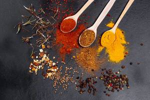 Spices in wooden spoons and scattered on a black background. Top view