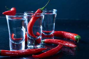 Spicy red chili with vodka glasses on black background