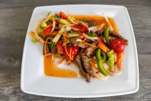 Spicy Thai food with beef, healthy vegetables, onions, carrots and fish soup on a white plate on a wooden table
