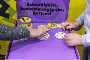 SPIEL 19 in Essen: zwei Besucher spielen Beobachtungs- und Reaktionsspiel "Dobble" mit runden Karten, die jeweils acht Symbole zeigen