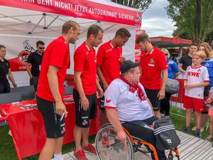 Spieler des 1. FC Köln posieren für Fotos mit einem Fan im Rollstuhl