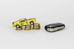 Spielzeugauto auf aufeinander gestapelten Münzen und Autoschlüssel
