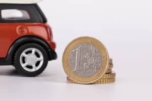 Spielzeugauto mit 1-Euro-Münze vor weißem Hintergrund
