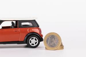 Spielzeugauto mit Euromünze vor weißem Hintergrund