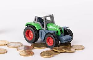 Spielzeugtraktor und Euro-Münzen vor weißem Hintergrund
