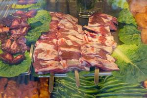 Spieße mit Schweinefleisch in einer Vitrine mit Salat und grünen Chilis