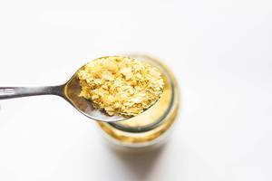 Spoon of vegan nutritional yeast flakes on white background