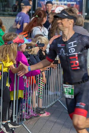 Sports enthusiasts and children behind security barriers high-five Ironman participants and runners on the marathon course in Lahti, Finland
