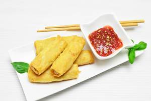 Spring rolls on a small plate with sweet and chilli sauce and sticks