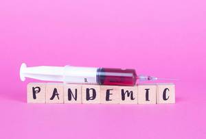 Spritze mit Blutprobe liegt auf dem Wort Pandemic zu Deutsch Pandemie auf Holzwürfeln