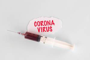 Spritze mit Blutprobe neben einem Zettel mit den Worten Corona Virus auf weißem Hintergrund