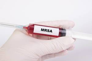 Spritze mit Injektionsnadel und dem Text MRSA - Methicillin resistenter Staphylococcus aureus
