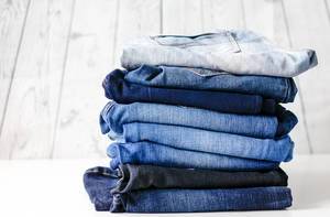 Stack of different colored Jeans on white wooden background